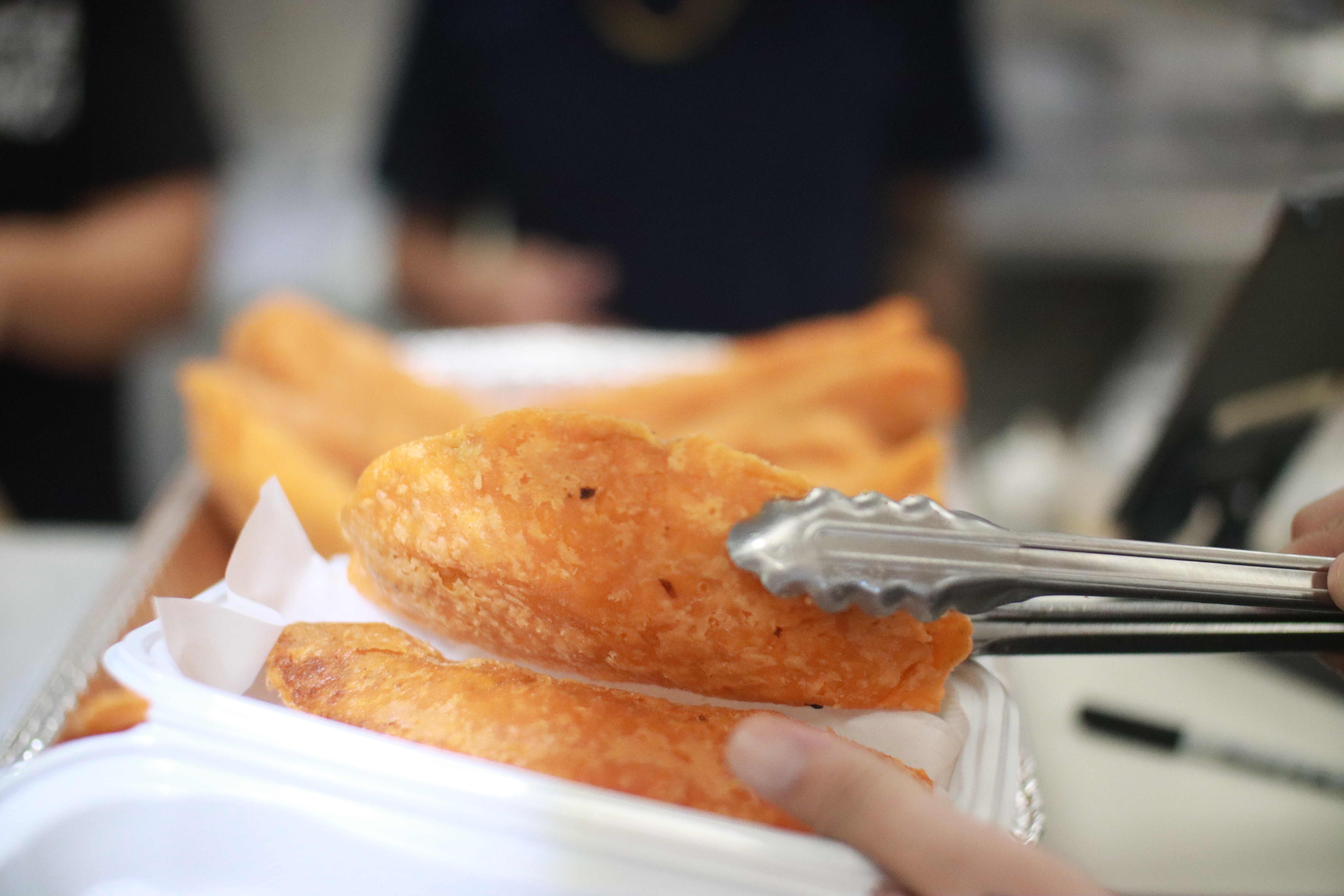 Close-up of crispy golden empanada held with tongs